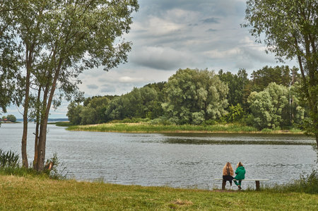 Two girls are sitting on a bench on the shore of the bayの写真素材