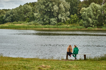 Two girls are sitting on a bench on the shore of the bayの写真素材