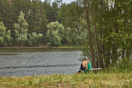 Two girls are sitting on a bench on the shore of the bayの写真素材