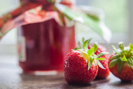 strawberry jam glass and berries in window light homemadeの写真素材