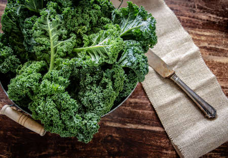 Green kale in basket and knife on wooden background on daylight