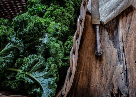 Green kale in basket and knife on wooden background