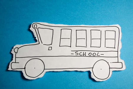 SKETCH made by a child, little School bus draw on a cut out white piece of paper shot on a bright Cyan blue backgroundの写真素材