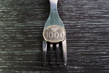 Rupiah coin on fork on black wooden texture background
