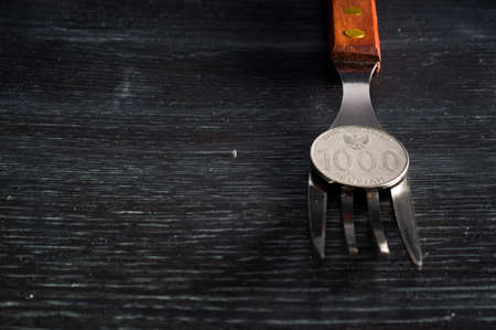 Rupiah coin on fork on black wooden texture background
