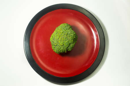 Green Brocolli on Red and Black Plate on White Backgroundの写真素材