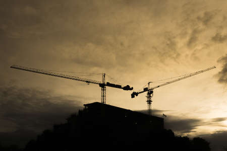 Sillhouette of building construction with two crane on morning yellow skyの写真素材