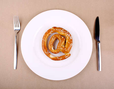 Fresh Pretzel in at sign with cutlery on white plateの写真素材