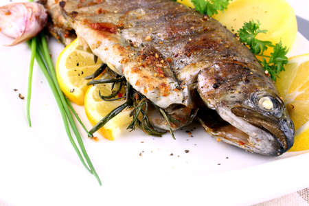 Grilled whole trout with potato, lemon and garlic, close up