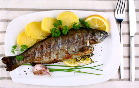Grilled whole trout with potato, lemon and garlic, top view