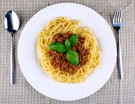 Delicious spaghetti bolognese with basil on white plate, top view