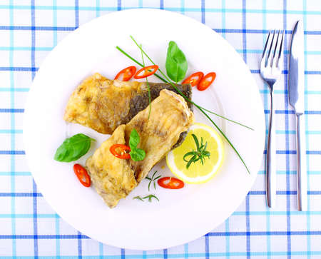 Two fried fish fillets with lemon slice on white plate, top view