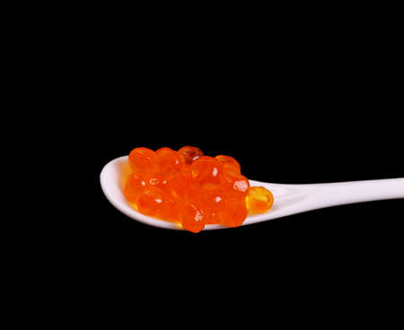 Porcelain spoon full of red salmon caviar on black background, close upの写真素材