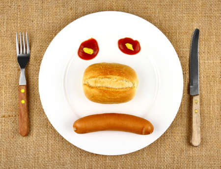 Sausage with bun on the plate as sad Face, top viewの写真素材