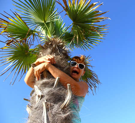 Mature woman sits on palm tree, scared, from underの写真素材