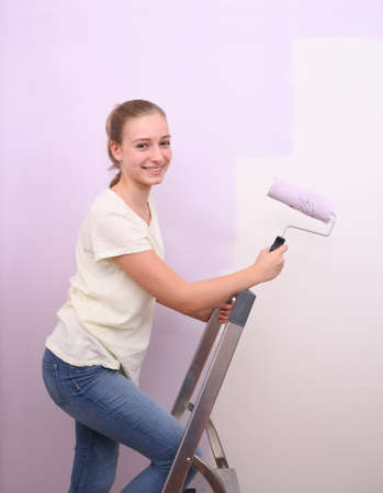 Girl paints wall in lilac color with roller, horizontalの写真素材