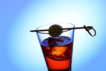 drink glass with red liquid, olive, ice cubes on blue backgroundの写真素材