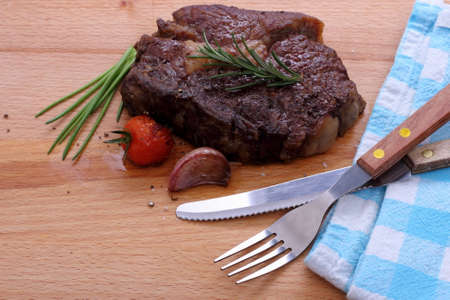 Rib eye steak, cherry tomatoes, garlic, herbs on wooden backgroundの写真素材