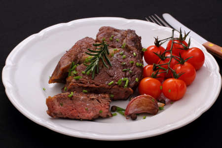 Rib eye steak, cherry tomatoes, garlic, herbs on black backgroundの写真素材