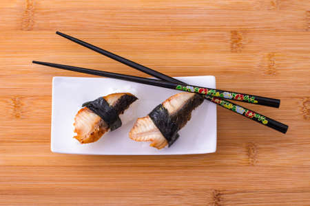 Two nigiri eel sushi with chopstick on bamboo board top viewの写真素材