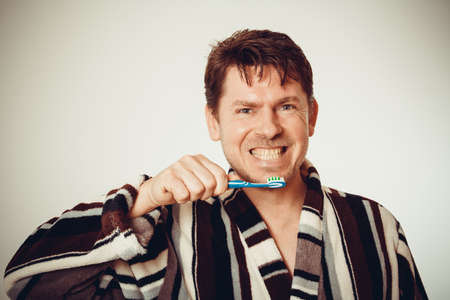 Good-humored man in bathrobe brushing teeth in vintage lookの写真素材