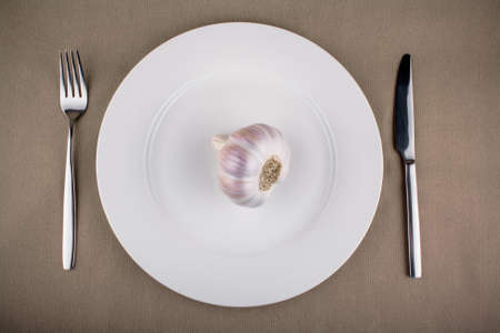 Garlic on white plate with fork and knife, top viewの写真素材