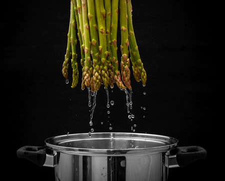 Green asparagus bundles with water flowing in metal pot, black backgroundの写真素材