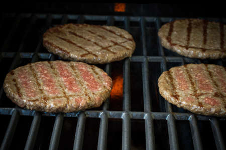 Four beef hamburger slices on grill rack, soft focus, close upの写真素材
