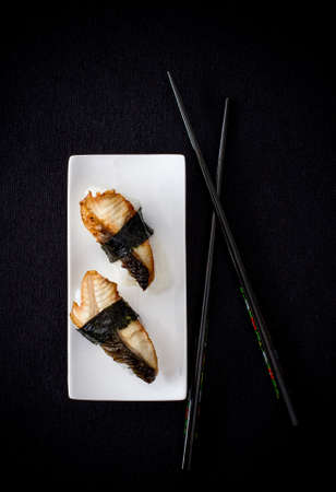 Two nigiri eel sushi with chopstick on black background, top view