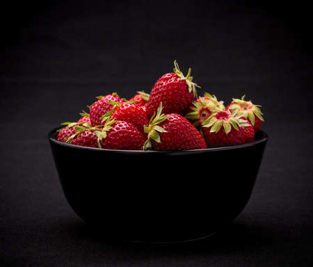 Ripe fresh strawberry in bowl on black background, close upの写真素材