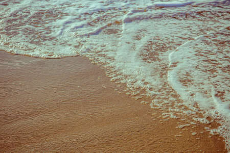 Soft foam wave of sea on sandy beach close up as backgroundの写真素材