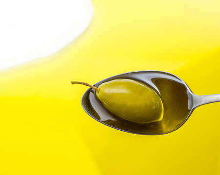 Green olive in full oil spoon on yellow background, top viewの写真素材