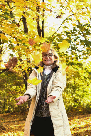 Portrait of mature attractive woman playing with autumnの写真素材