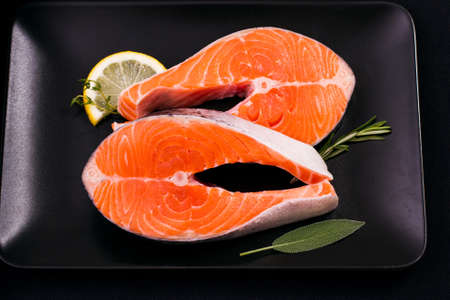 Two delicious raw salmon slice with spices on black plate, top viewの写真素材