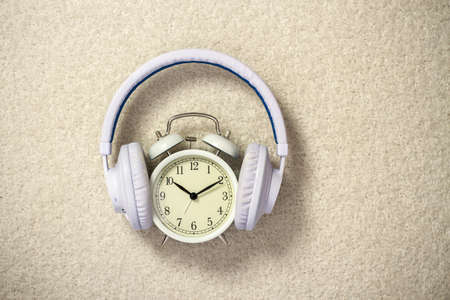 Retro alarm clock with white headphones on beige background