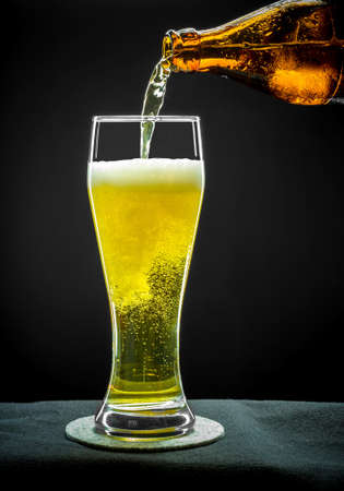 Filling glass glass with golden beer on black backgroundの写真素材