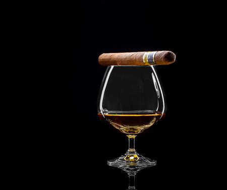Cognac swivel with golden alcohol and cigar on black backgroundの写真素材
