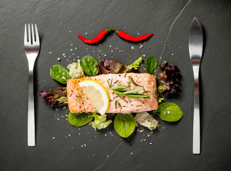 Grilled salmon fillet with salad on black slate plate, top viewの写真素材