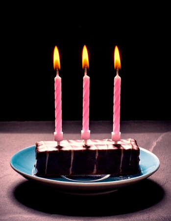 Chocolate cake with three pink candles on blue plate, black backgroundの写真素材