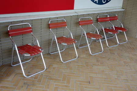 Five folding chairs are lined up against a wall, with a patterned floor.の写真素材