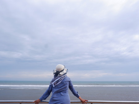 Woman wearing a white hat standing on the balcony and looking at the seaの写真素材