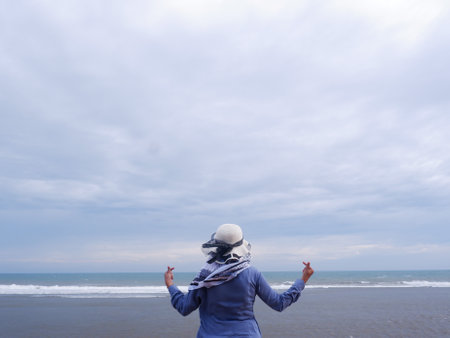 Asian woman wearing hijab standing on the beach and looking at the sea.の写真素材