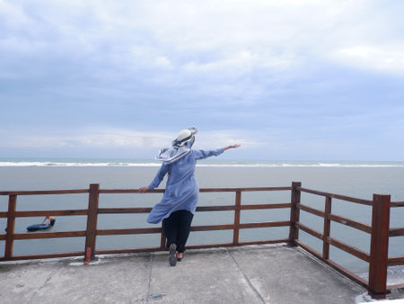 A woman wearing a blue raincoat is standing on the railing.の写真素材
