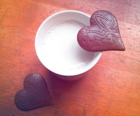 Two Heart-shaped pieces of chocolate on a cup of milkの写真素材