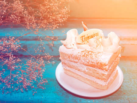 A piece of tiramisu cake in warm light on blue wooden background