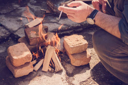 Man relaxing near fire, smoking. Warm vintage filter applied.