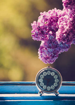 Branch of lilac flower on vintage elegant clock at the window. Natural light.の写真素材