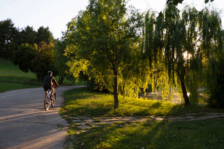 Bucharest, ROMANIA - June 22, 2015: One man riding his bycicle in sunset light in Tineretului park, Bucharest. BUCHAREST -June 22, 2015のeditorial素材