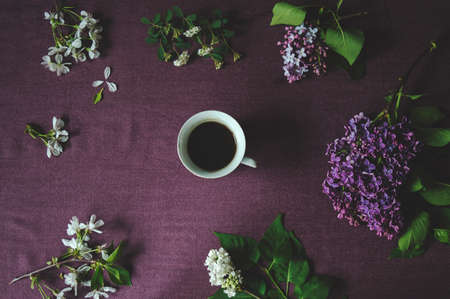 Coffee cup on dark purple table with various spring flowers. Flat lay.の写真素材