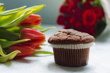 Simple chocolate muffin against roses and tulips in the background.の写真素材